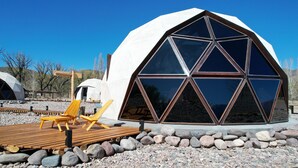 A geodesic dome structure with a large glass window, surrounded by a wooden deck and outdoor seating. - Cinco Cumbres luxury Camp & Eco Lodge (Uspallata)