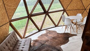 A geodesic dome interior with a dining area, a leather sofa, and a view of the outdoors. - Cinco Cumbres luxury Camp & Eco Lodge (Uspallata)