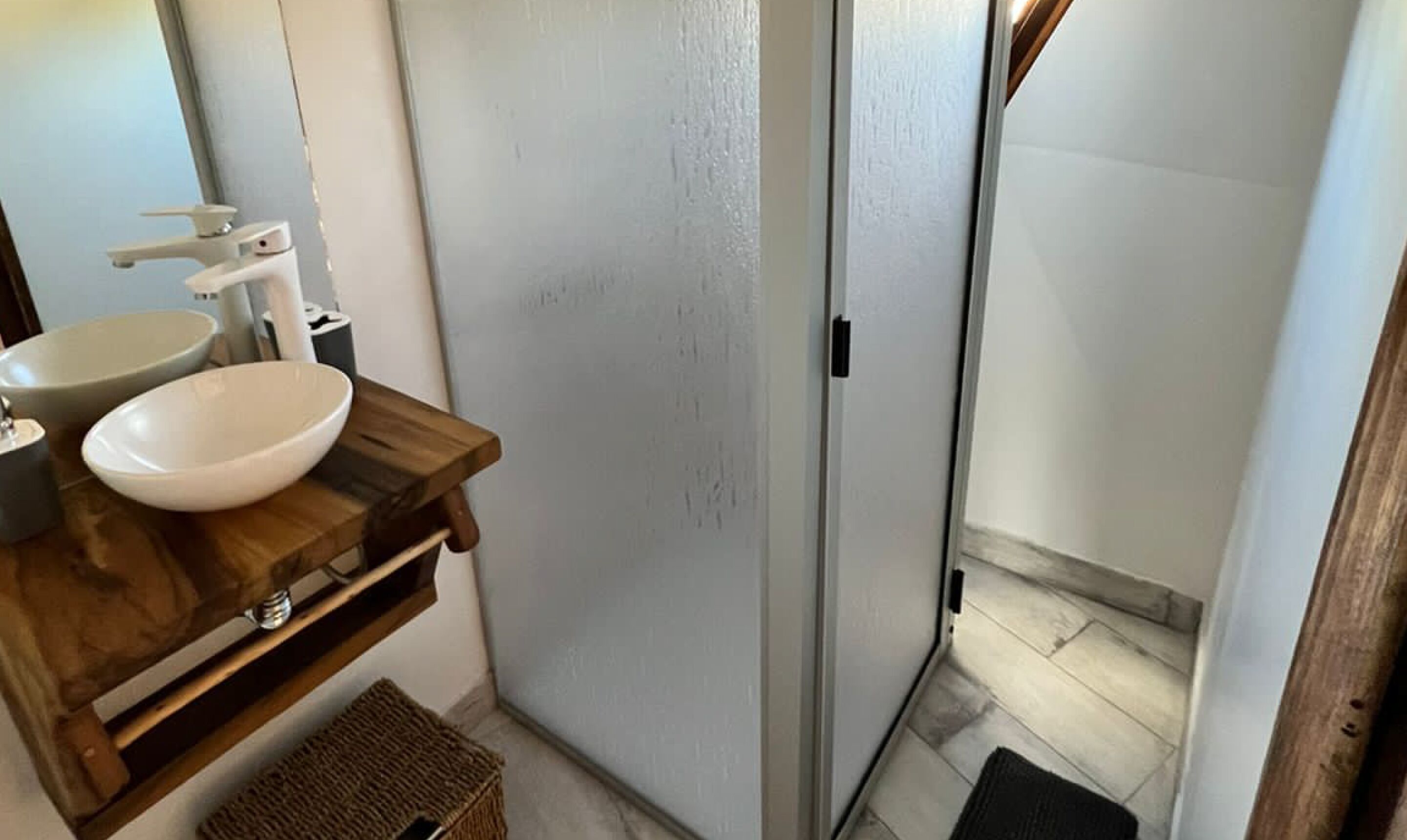 Ein Badezimmer mit einem Holzbidet, einem weißen Waschbecken und einer Glasdusche.
