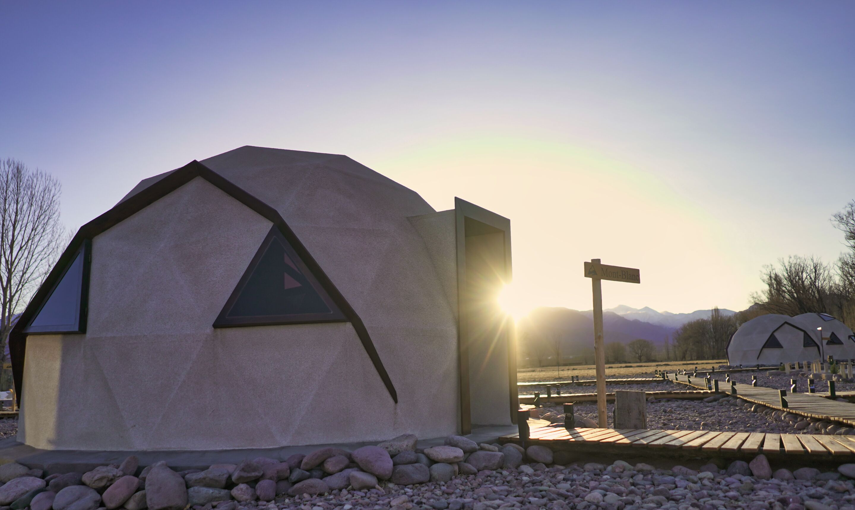 A geodesic dome structure with a triangular entrance, a signpost labeled "Mont-Blanc", and a wooden deck leading to it.