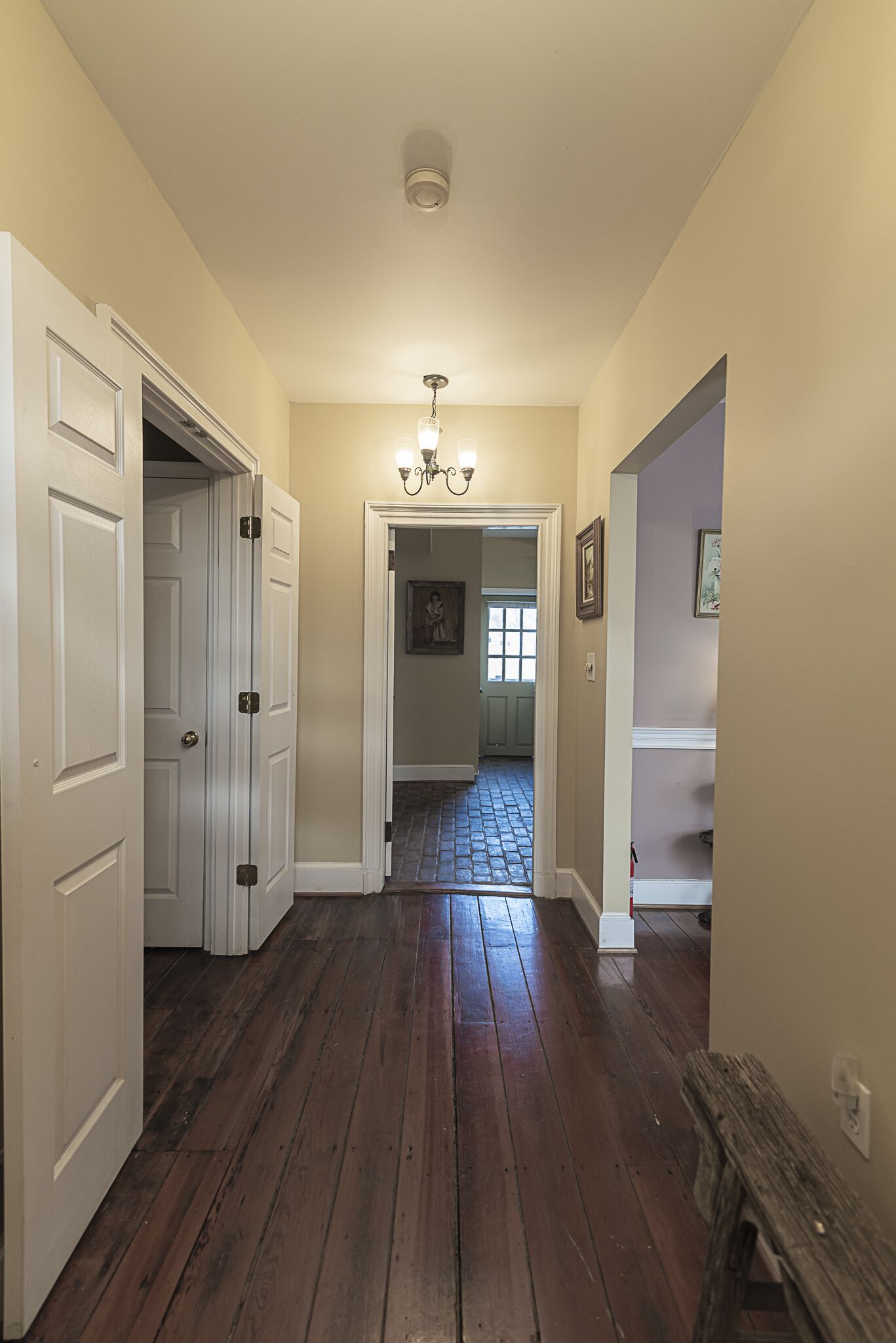 A hallway with wooden flooring, white walls, and a ceiling light fixture.