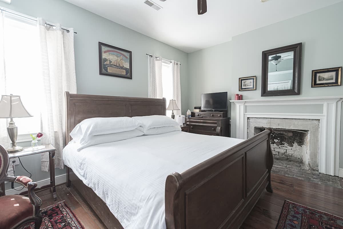 A bedroom with a wooden bed, a television, a fireplace, and a window with curtains.