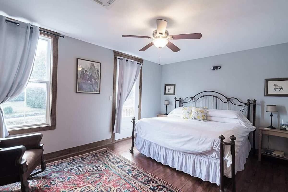 A bedroom with a bed, a ceiling fan, a nightstand, a chair, a window with curtains, and a rug.
