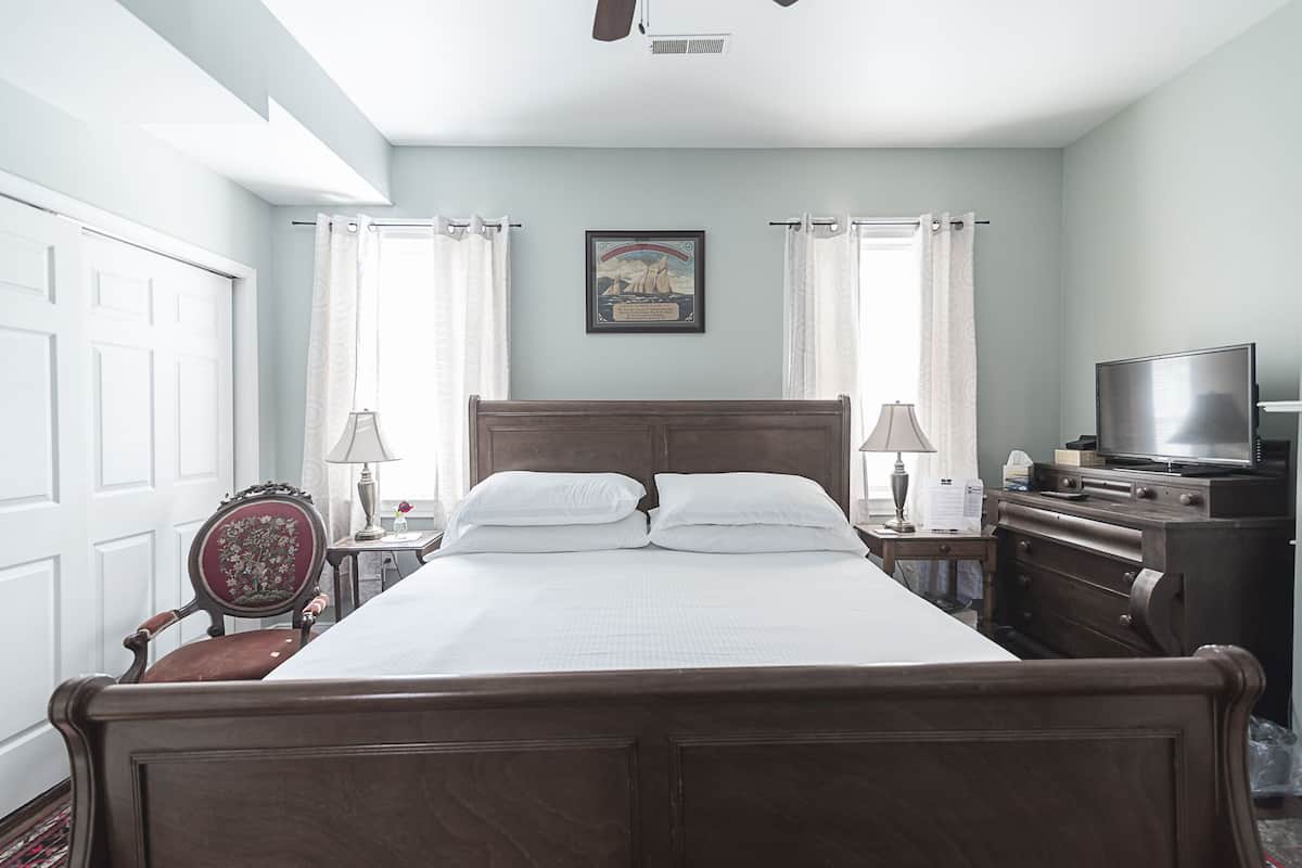 A neatly arranged bedroom with a large bed, two bedside tables with lamps, a television, and a chair.