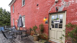 A red brick building with a white door, a welcome sign, and outdoor seating with metal chairs and tables. - Light Horse Inn (Harpers Ferry)