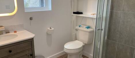 A modern bathroom with a toilet, a sink, a glass shower enclosure, and a towel rack with neatly folded towels.