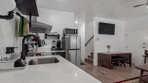 Une cuisine moderne équipée d’un réfrigérateur, d’un four à micro-ondes et d’un évier en acier inoxydable. On y trouve une table à manger en bois et un escalier menant à un autre niveau.