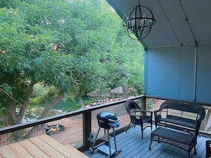 A balcony with a grill, wicker furniture, and a view of a river and trees. - 6 Son's Rio Cibolo - Birdhouse Cabin (Marion)