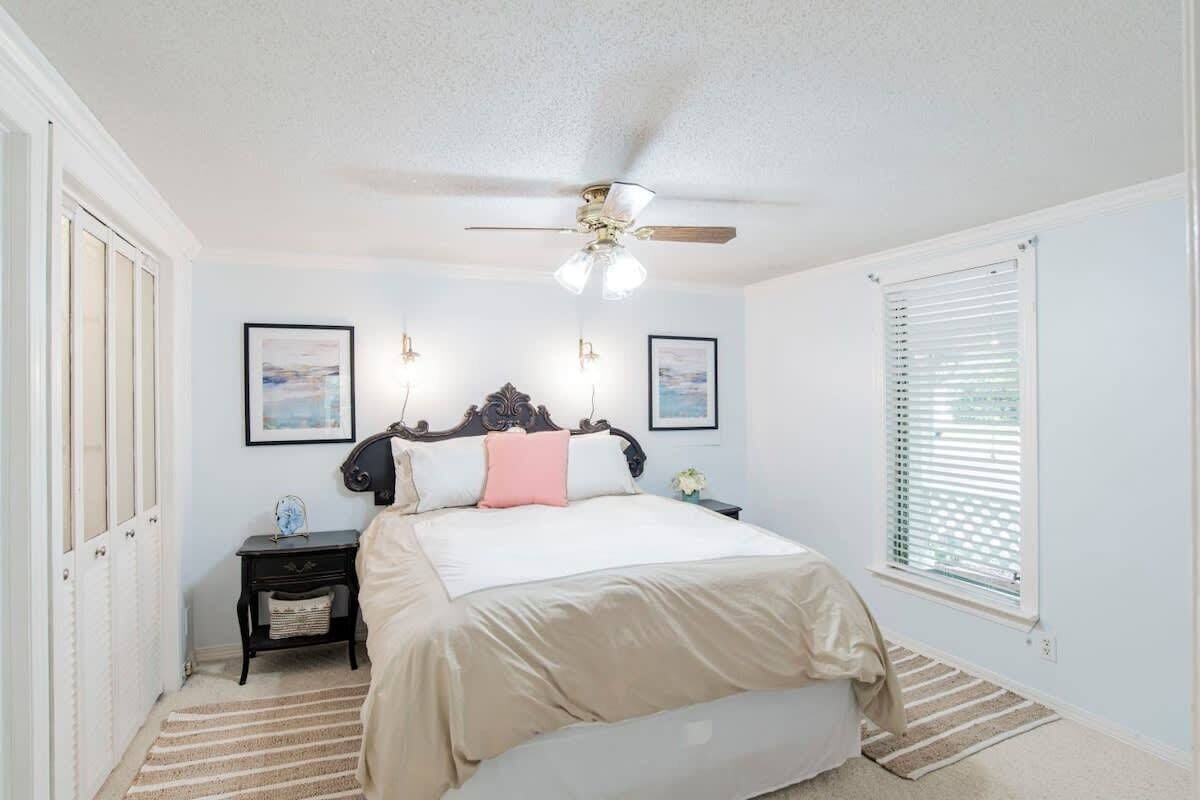 A bedroom with a bed, a nightstand, a ceiling fan, and a window with blinds.