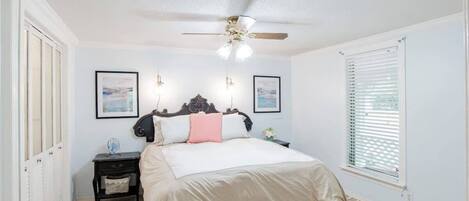 A bedroom with a bed, a nightstand, a ceiling fan, and a window with blinds.