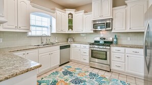A kitchen with white cabinets, a granite countertop, a stainless steel refrigerator, a microwave, an oven, and a dishwasher. - Blue Mermaid! Beautiful home 4 blocks from the beach! (Galveston)