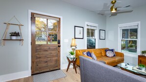 Ein Wohnzimmer mit Holztür, einer Couch, einem Glastisch und einem Deckenventilator.