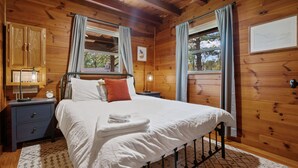 Een houten slaapkamer met een bed, nachtkastjes en een raam met gordijnen.