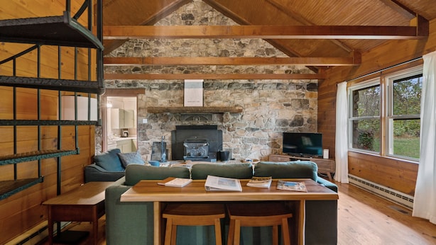 Een gezellig interieur van een chalet met een stenen openhaard, houten balken, een bank, een tafel met stoelen en een televisie.
