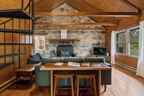 Interior acollidor d'una cabana amb una llar de pedra, bigues de fusta, un sofà, una taula amb cadires i una televisió.