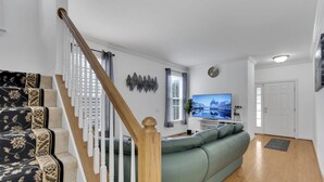 A living room with a staircase, a green sofa, a television, and a decorative wall piece.