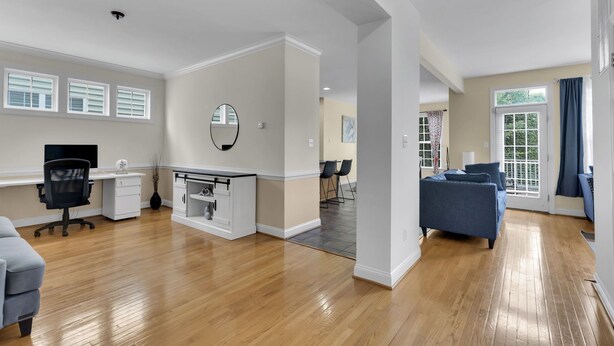 A spacious living area with a wooden floor, a dining area, a kitchen, and a large window with curtains.