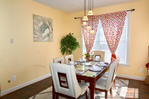 A dining area with a table set for four, surrounded by chairs, a potted plant, and a painting on the wall.