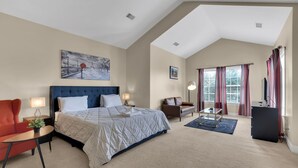 A hotel room with a large bed, a desk, a chair, a TV, and a painting on the wall.