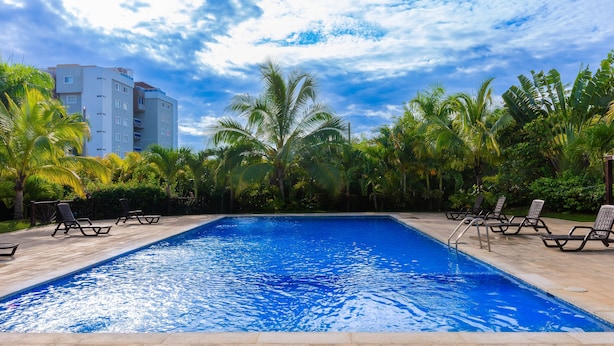 Ein Pool mit Liegestühlen, umgeben von Palmen und einem Gebäude im Hintergrund.