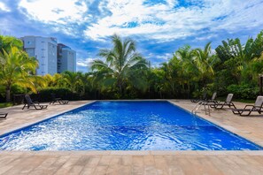 A swimming pool with lounge chairs, surrounded by palm trees and a building in the background. - Modern Apt With free parking and AC 3brs (Puñal)