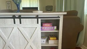 Un gabinete de madera con diseño de puerta de granero, que contiene juegos de mesa y una lámpara.