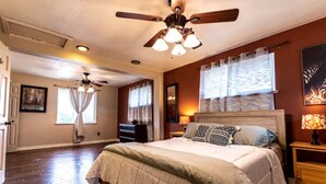 Un dormitorio con una cama grande, un ventilador de techo y una ventana con cortinas.