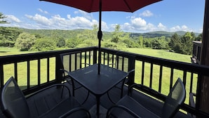 A deck with a table and chairs, a red umbrella, and a view of a green landscape with trees and hills.