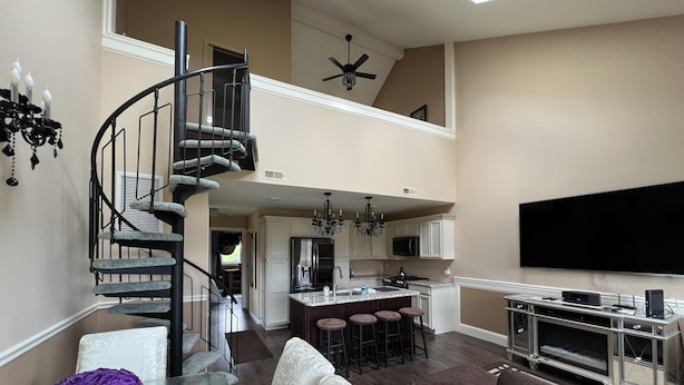 A spacious living area with a central island, a spiral staircase, a flat-screen TV, and a modern kitchen.