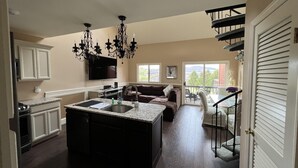A spacious kitchen with a large island, dark wood flooring, and a chandelier.