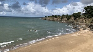 Una playa arenosa con olas suaves, un acantilado rocoso y cielo despejado.
