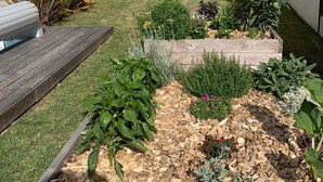 Un patio trasero con terraza de madera, jardineras elevadas y valla de madera.