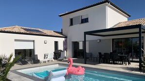 Una casa moderna con piscina, mobiliario exterior y una zona de patio techada.