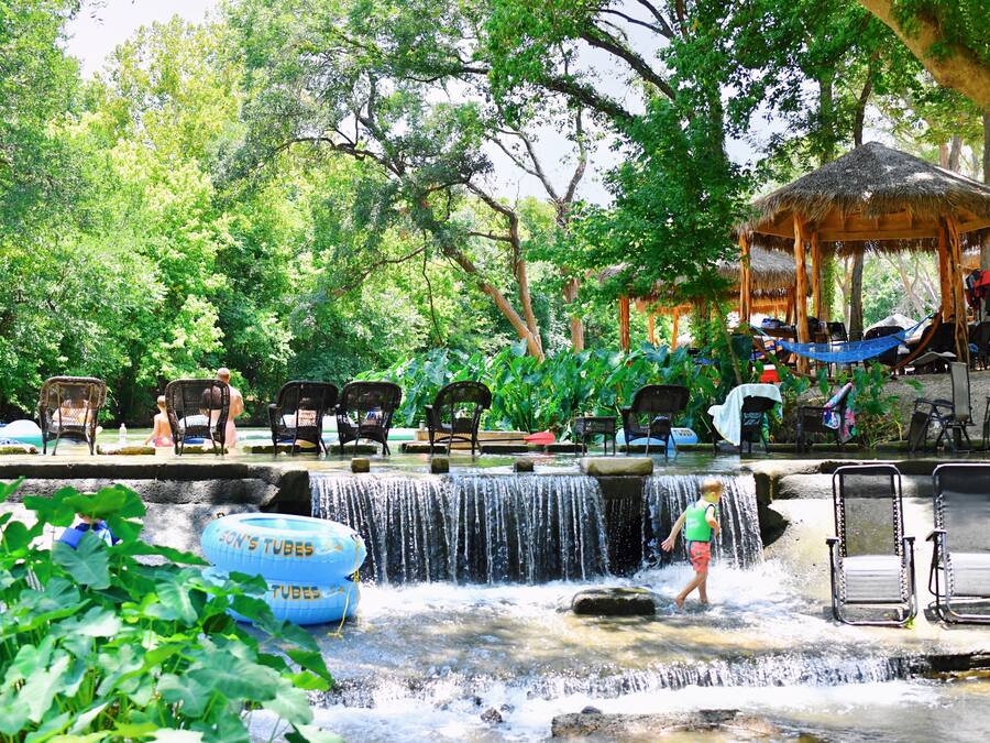 A water feature with chairs and a thatched-roof structure in a lush, green setting.