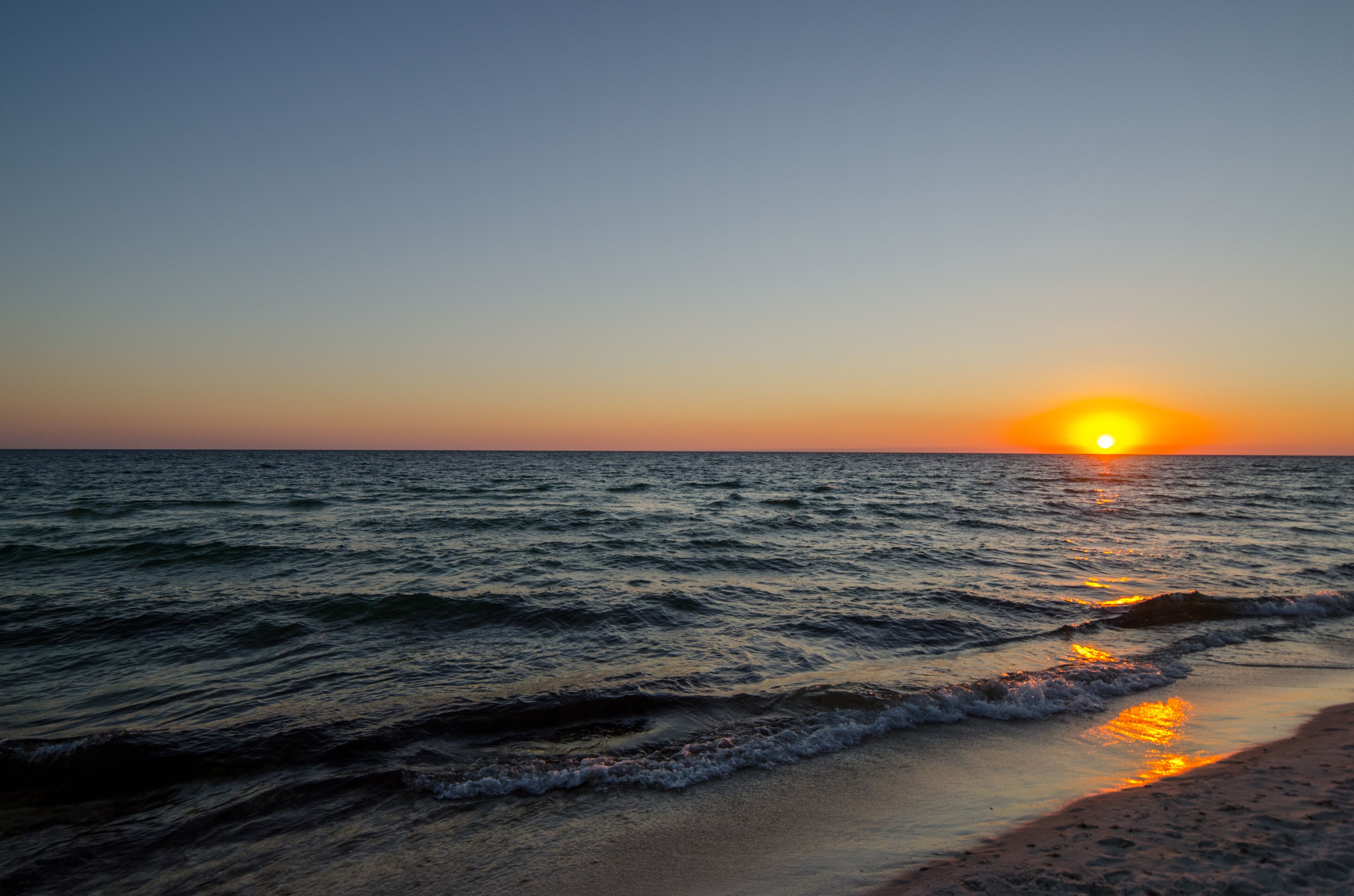 A sunset over the ocean with waves gently touching the shore.