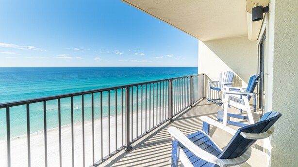 A balcony with a view of the ocean, a railing, and two blue chairs.