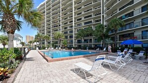 A hotel with a swimming pool, lounge chairs, and palm trees.