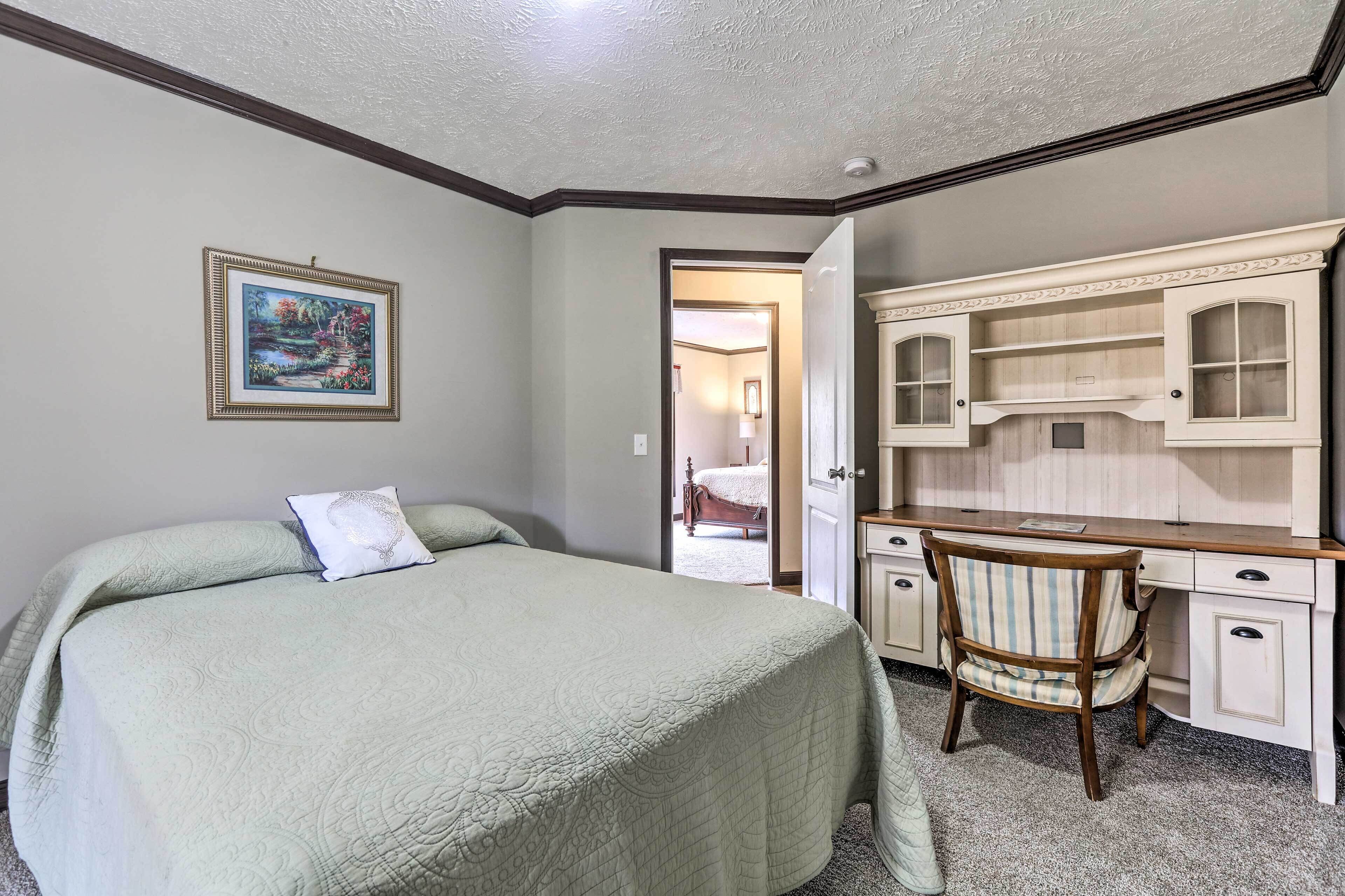 A bedroom with a bed, a desk, and a chair. There is a door leading to another room.