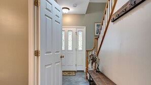 A hallway with a white door, a wooden bench, and a staircase with a wooden railing.