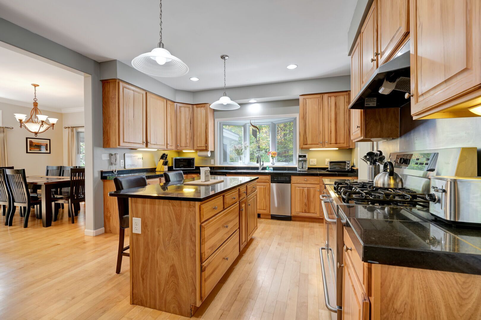 A modern kitchen with wooden cabinets, a central island, stainless steel appliances, and pendant lighting.