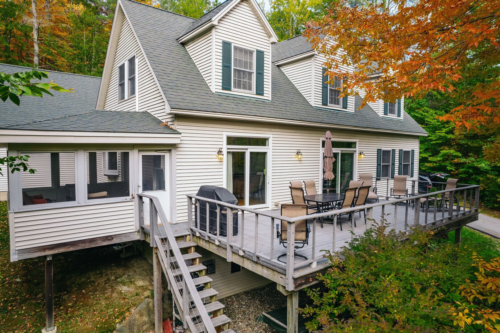 Ein zweistöckiges Haus mit einer Terrasse, Sitzgelegenheiten im Freien und einer Treppe, die zu einer Veranda führt.