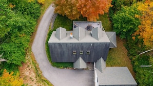 A large, dark-colored building with a flat roof, a driveway, and a surrounding area with trees in autumn colors.