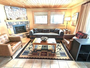 A living room with a stone fireplace, a sofa set, a coffee table, and a patterned rug.