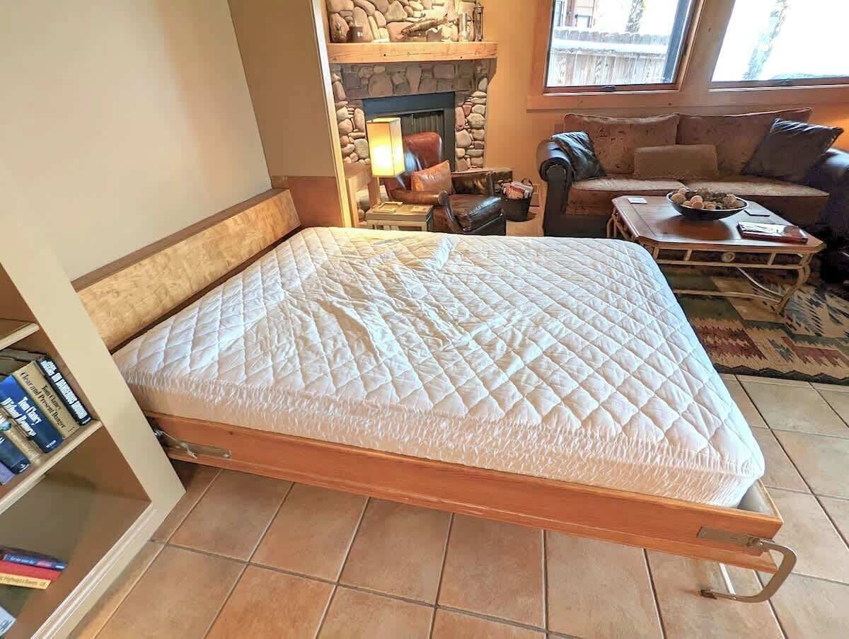 Ein Bett mit einer gesteppten Matratze in einem Zimmer mit Kamin aus Stein, einem Ledersofa und einem Holztisch.