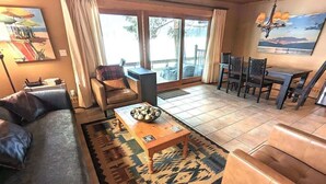 Een woonkamer met een bank, een salontafel, een eettafel met stoelen en een uitzicht door grote ramen.