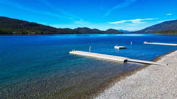 Een helder meer met een steiger die het water in loopt, omgeven door bergen en heldere luchten.