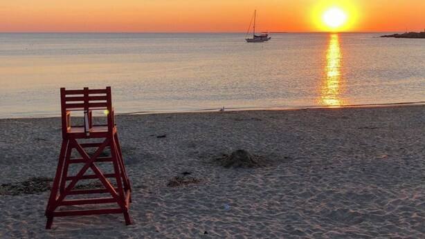 Una playa con un puesto de salvavidas y un barco a lo lejos durante el atardecer.