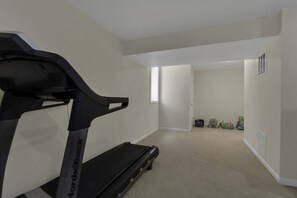 Una habitación con una cinta de correr, una ventana y una puerta que da a otra estancia.