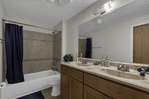 Un baño moderno con bañera, dos lavamanos, inodoro y un espejo grande.
