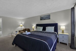 Una habitación de hotel con una cama grande, dos mesitas de noche con lámparas, un sillón de cuero marrón y un cuadro en la pared.